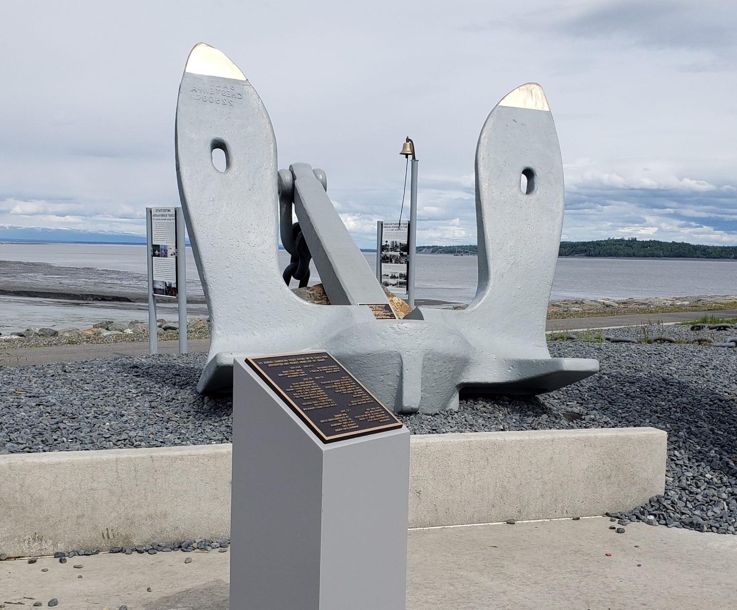 Anchor for the USS Anchorage sits on small rocks with commemorative plaque in the foreground. 